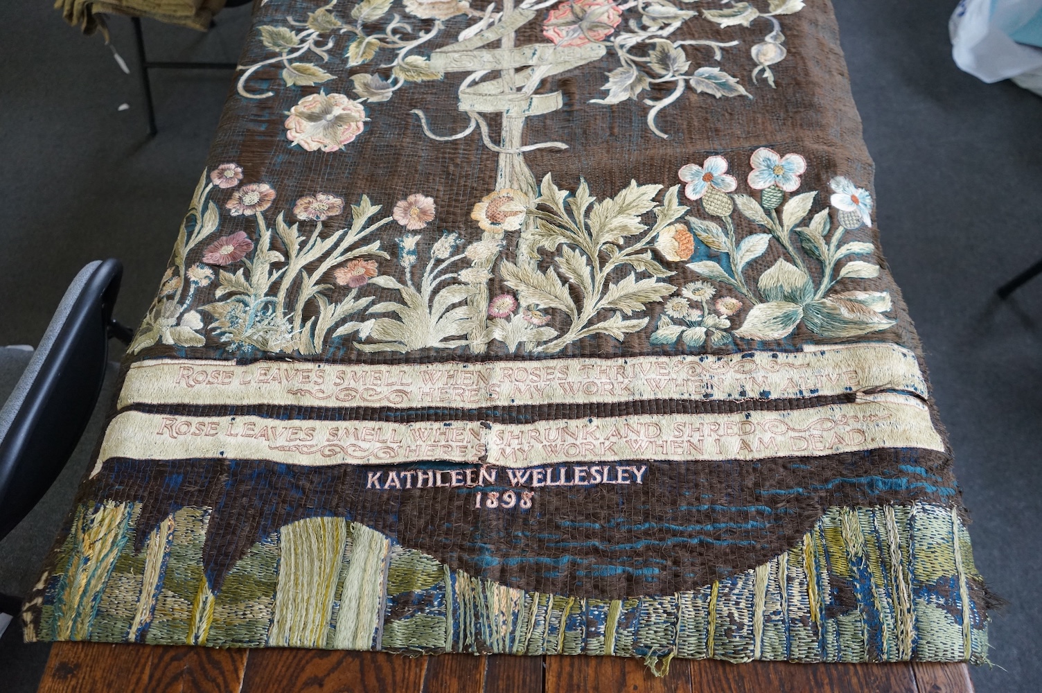 A large Arts and Crafts silk embroidered wall hanging, embroidered in the manner of May Morris with a large central scrolling flowering rose tree and banner embroidered with Salve and a two row motto below;, Rose leaves